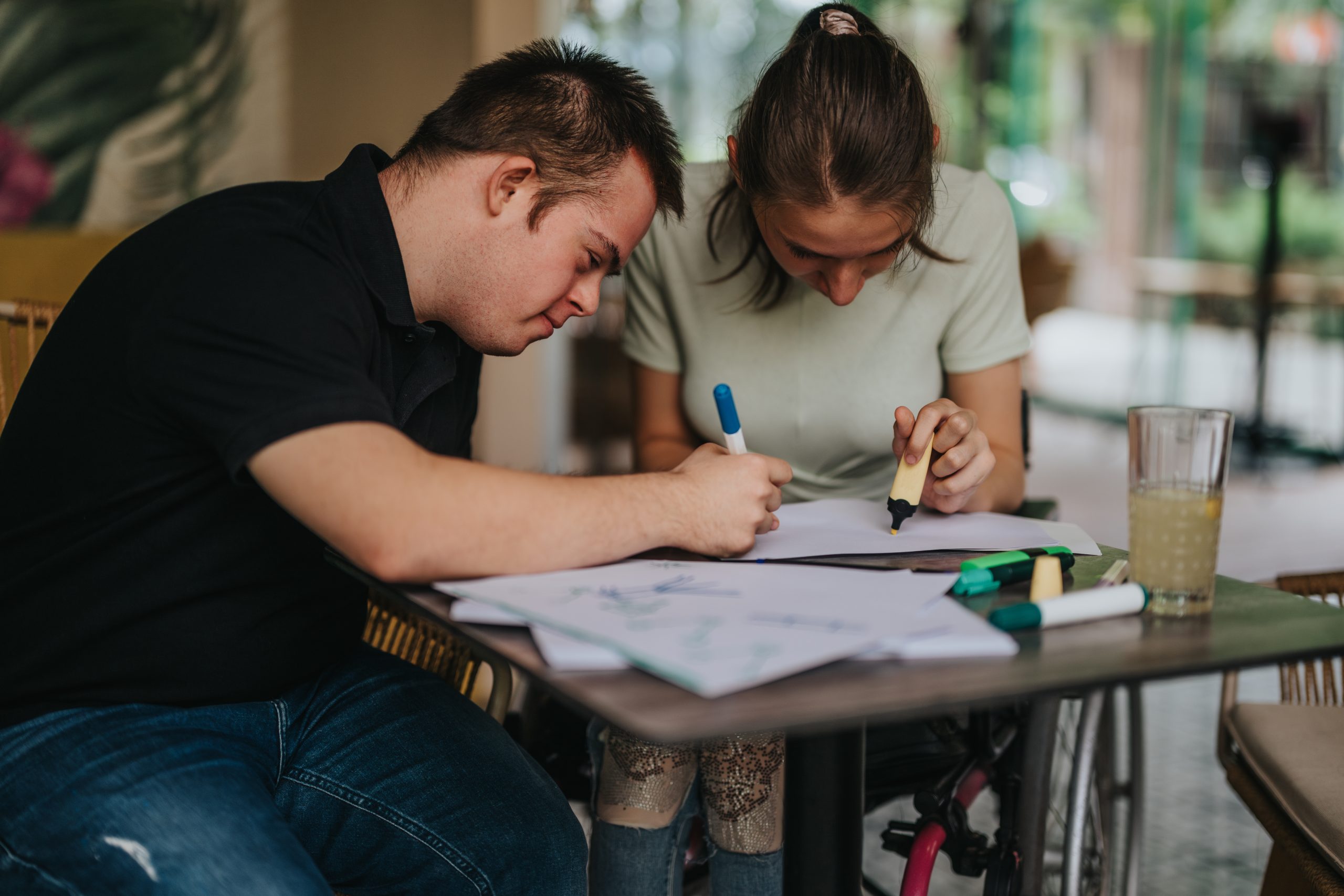 Young man with Down syndrome drawing at a table with a friend during an NDIS support session in Geelong